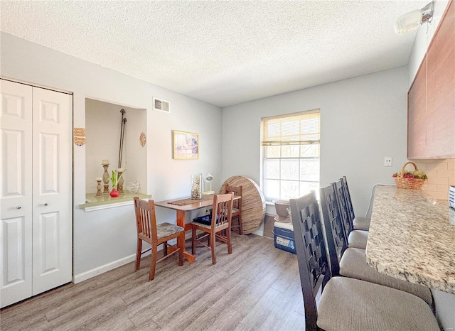 dining area with baseboards, light wood-style flooring, visible vents, and a textured ceiling