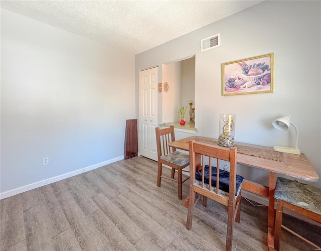 dining room featuring a textured ceiling, light wood-style flooring, visible vents, and baseboards