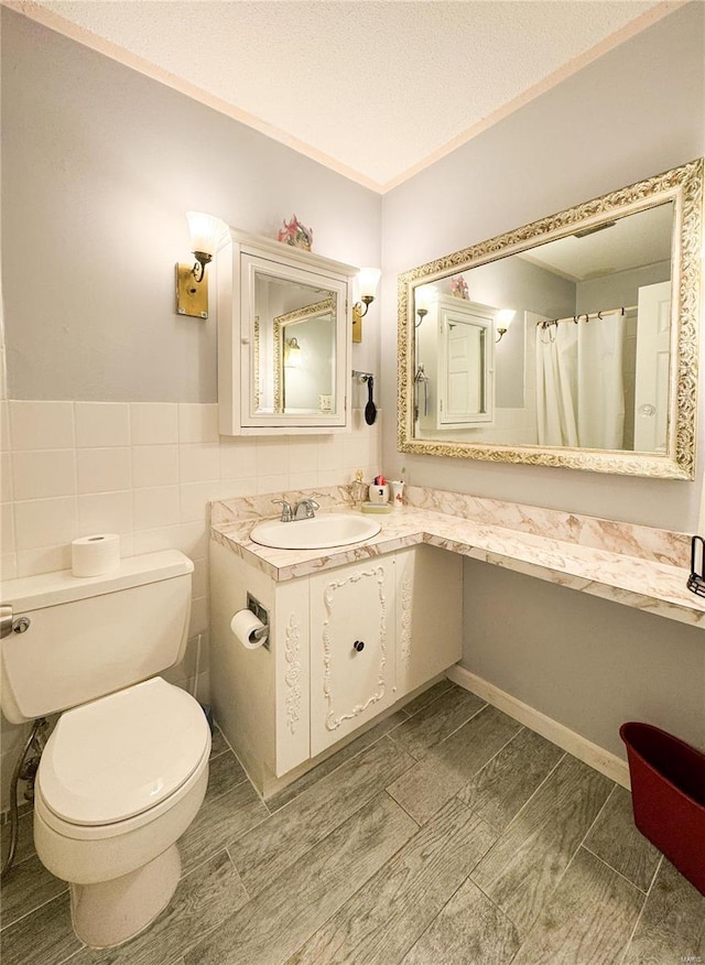 full bathroom with a wainscoted wall, tile walls, toilet, vanity, and a textured ceiling