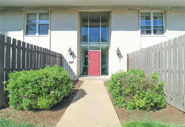 view of exterior entry with brick siding and fence