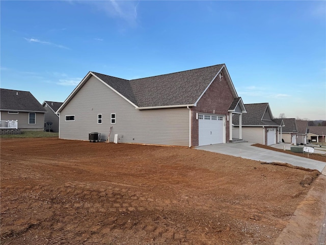 view of property exterior with a garage, brick siding, central AC, and driveway