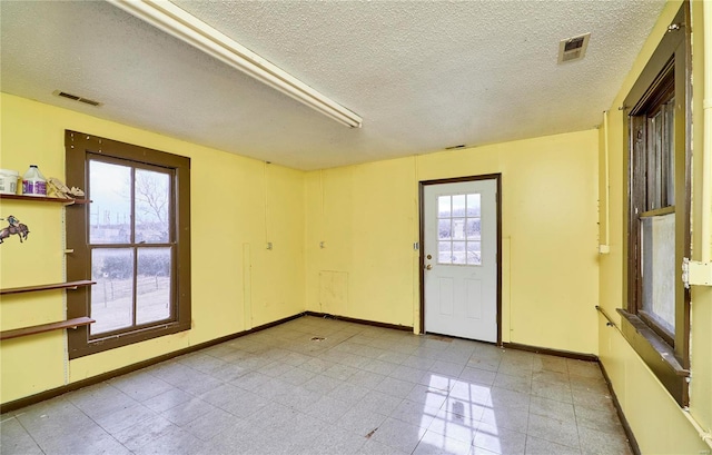 spare room featuring baseboards, visible vents, and a textured ceiling