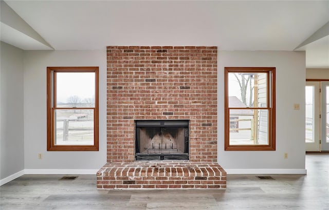 unfurnished living room featuring baseboards, plenty of natural light, wood finished floors, and a brick fireplace