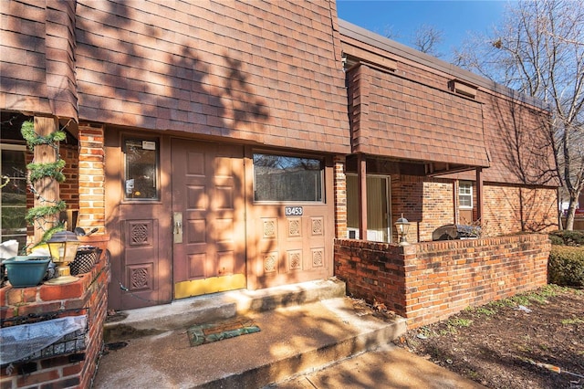 property entrance featuring brick siding, roof with shingles, and mansard roof