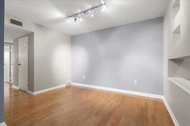 spare room featuring rail lighting, light wood-style floors, visible vents, and baseboards