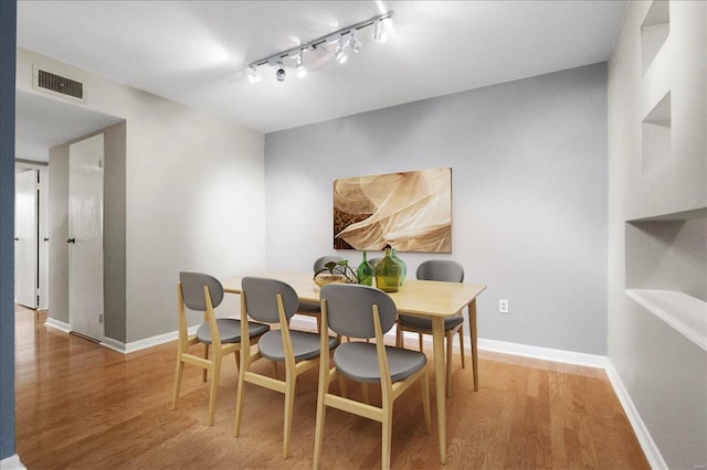 dining room featuring visible vents, rail lighting, baseboards, and wood finished floors