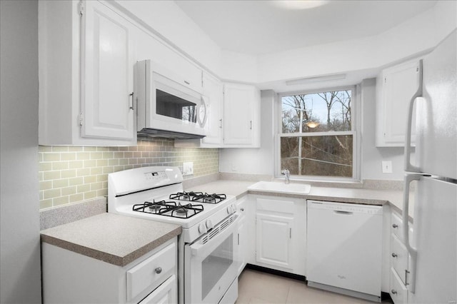 kitchen with white appliances, white cabinets, backsplash, and a sink