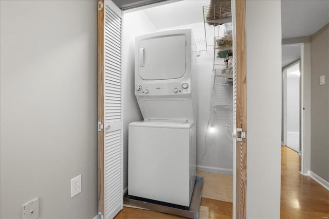 laundry room featuring laundry area, wood finished floors, stacked washer and clothes dryer, and baseboards