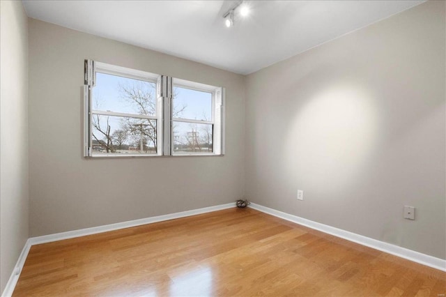 unfurnished room with baseboards, track lighting, and light wood finished floors