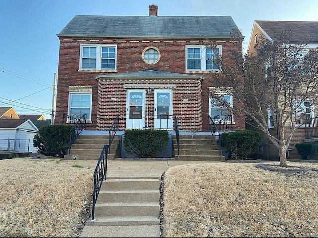 view of front of home featuring brick siding, a chimney, a front lawn, and stairway