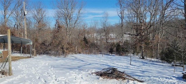 yard covered in snow featuring a forest view and a carport