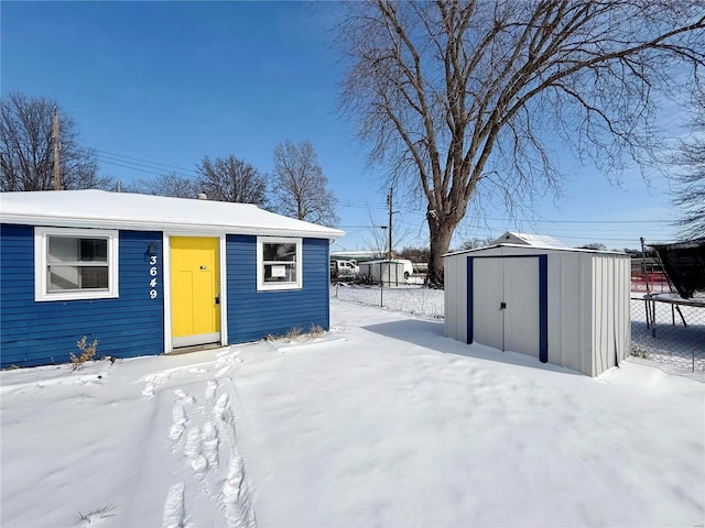 snow covered structure featuring an outbuilding, a storage shed, and fence