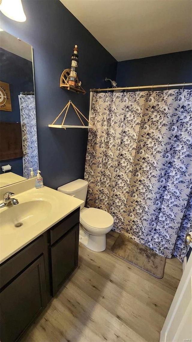 full bath with toilet, a shower with curtain, wood finished floors, and vanity