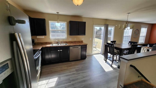 kitchen featuring dark cabinets, a sink, appliances with stainless steel finishes, light wood-type flooring, and decorative light fixtures