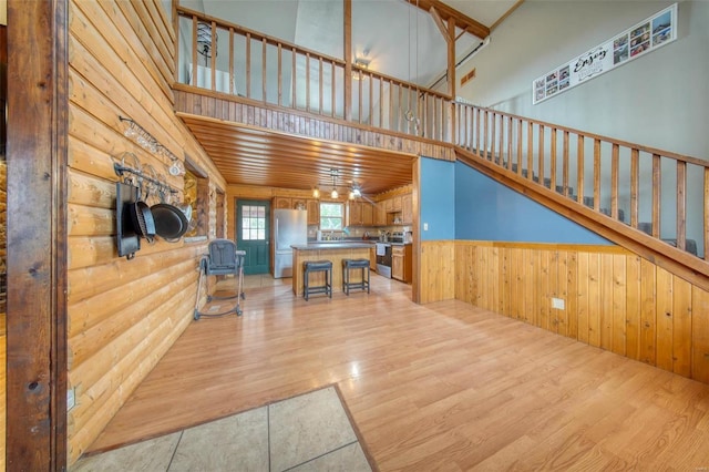 unfurnished living room with rustic walls, wainscoting, a towering ceiling, stairs, and light wood-type flooring