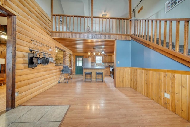 interior space featuring wainscoting, light wood finished floors, rustic walls, and a towering ceiling