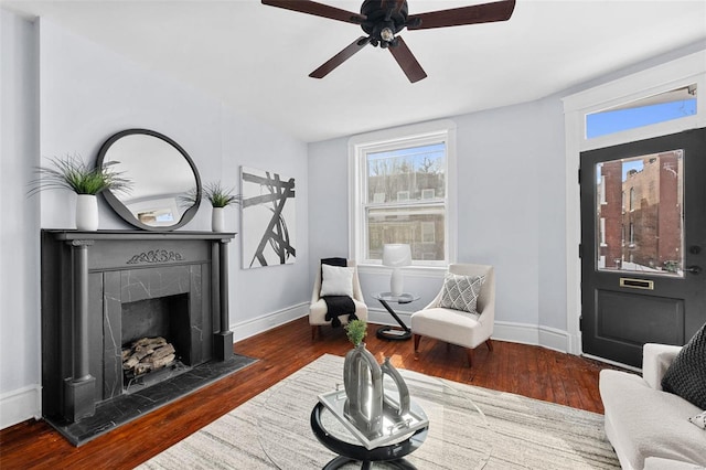 living area featuring a premium fireplace, baseboards, ceiling fan, and dark wood-type flooring