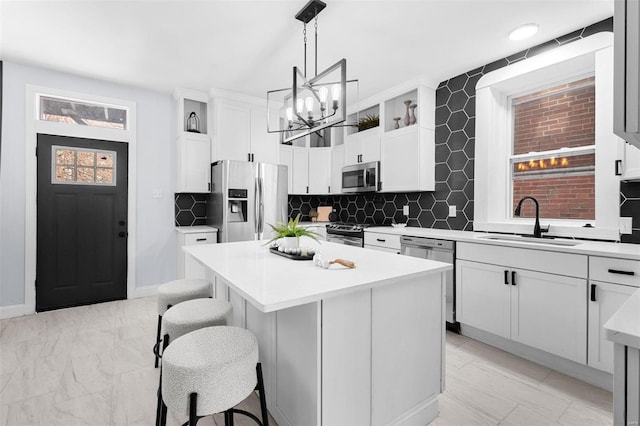 kitchen with a kitchen island, a sink, light countertops, appliances with stainless steel finishes, and white cabinets