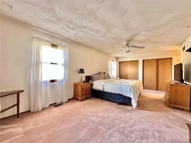 bedroom with light carpet, visible vents, a textured ceiling, and two closets