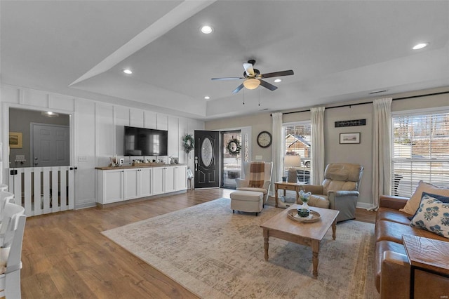 living room featuring light wood-style flooring, a tray ceiling, a ceiling fan, and recessed lighting