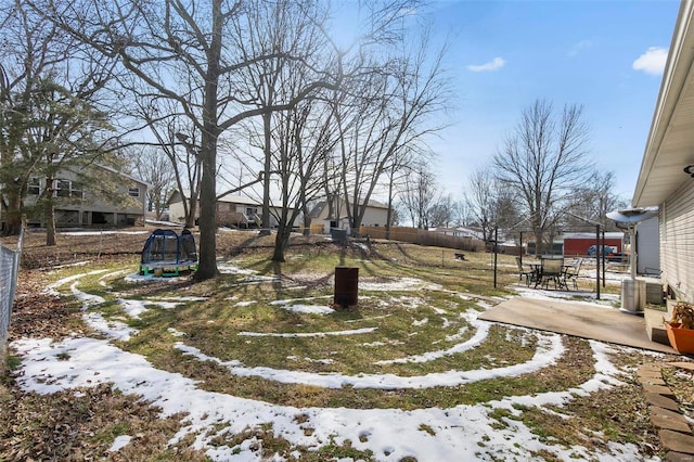 yard covered in snow with a trampoline, a patio area, and fence