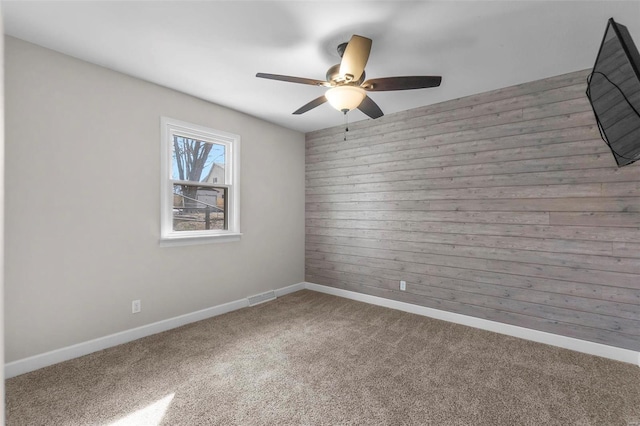 unfurnished room with carpet floors, visible vents, a ceiling fan, wood walls, and baseboards