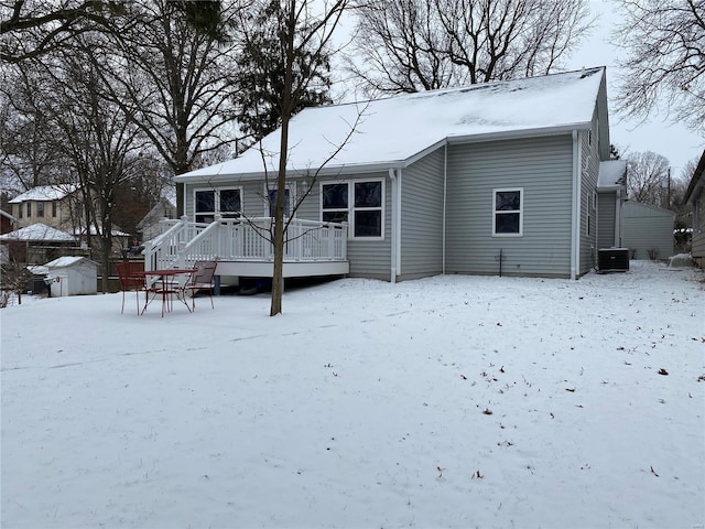 snow covered house featuring cooling unit, a deck, and a shed