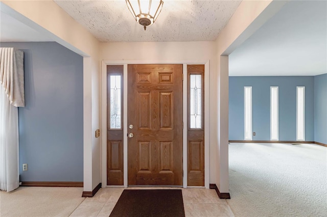 foyer entrance with light carpet, light tile patterned floors, and baseboards