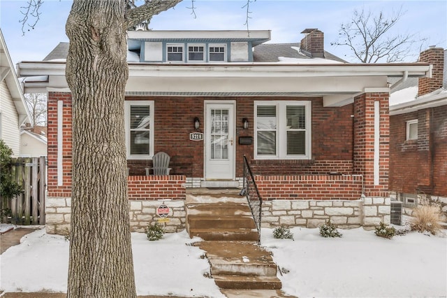 bungalow-style house featuring brick siding, a chimney, a porch, and fence