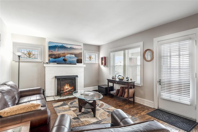 living area with a brick fireplace, baseboards, and dark wood-type flooring