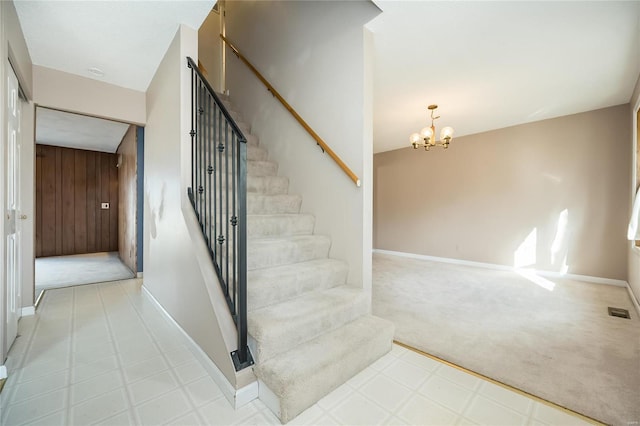 staircase featuring wooden walls, baseboards, carpet flooring, an inviting chandelier, and tile patterned floors