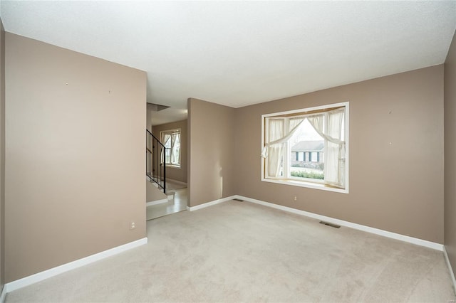 spare room featuring visible vents, baseboards, light colored carpet, and stairs