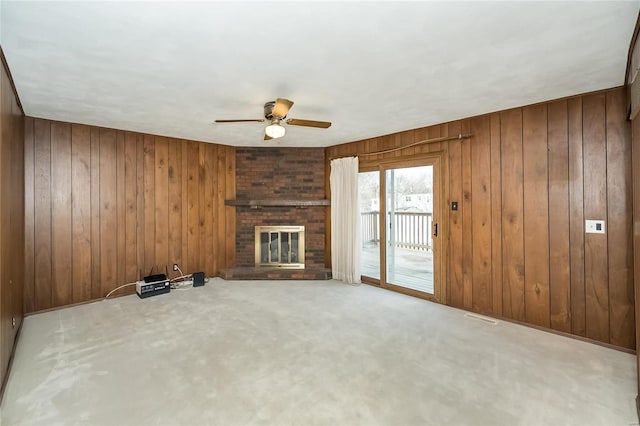 unfurnished living room featuring visible vents, wooden walls, a brick fireplace, and a ceiling fan