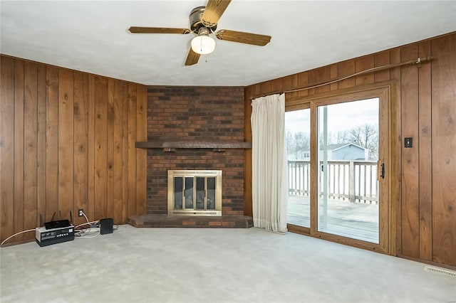 unfurnished living room featuring carpet flooring, wooden walls, a fireplace, and a ceiling fan