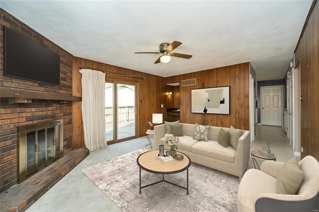 living area with a brick fireplace, wooden walls, visible vents, and ceiling fan