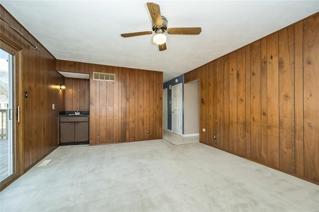 spare room featuring a ceiling fan, light colored carpet, visible vents, and wood walls