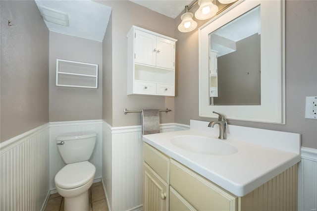 half bath featuring tile patterned floors, vanity, toilet, and wainscoting