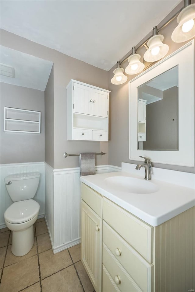 half bathroom featuring tile patterned floors, a wainscoted wall, toilet, and vanity