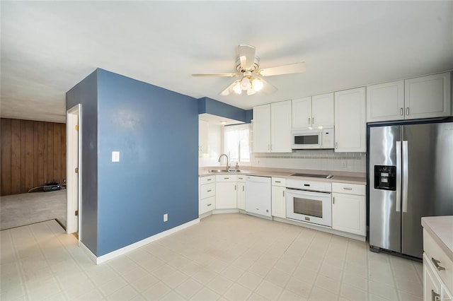 kitchen with a sink, white appliances, wooden walls, light countertops, and ceiling fan