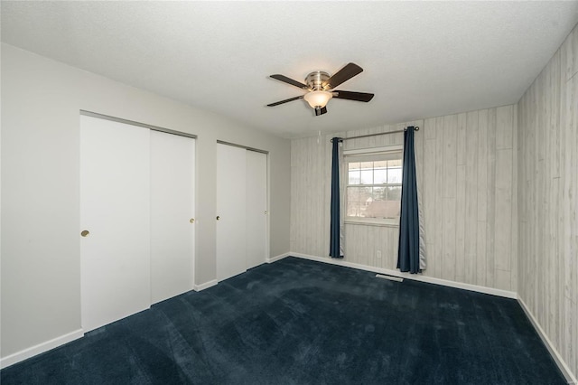 unfurnished bedroom with visible vents, two closets, ceiling fan, a textured ceiling, and dark carpet