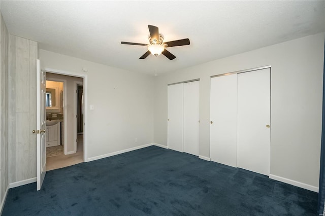 unfurnished bedroom with baseboards, multiple closets, a ceiling fan, and dark carpet