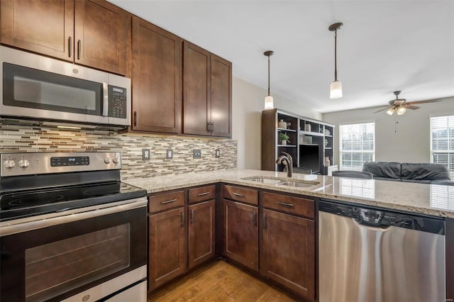 kitchen featuring light stone countertops, wood finished floors, a sink, stainless steel appliances, and backsplash