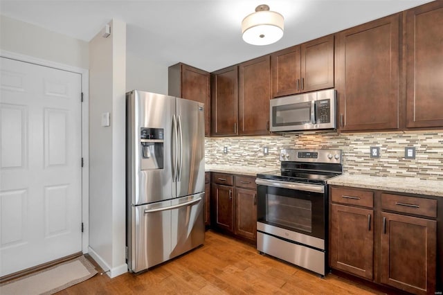 kitchen featuring tasteful backsplash, stainless steel appliances, light wood-style floors, and light stone countertops