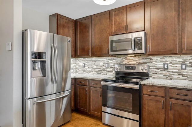 kitchen with light stone counters, backsplash, appliances with stainless steel finishes, and light wood finished floors