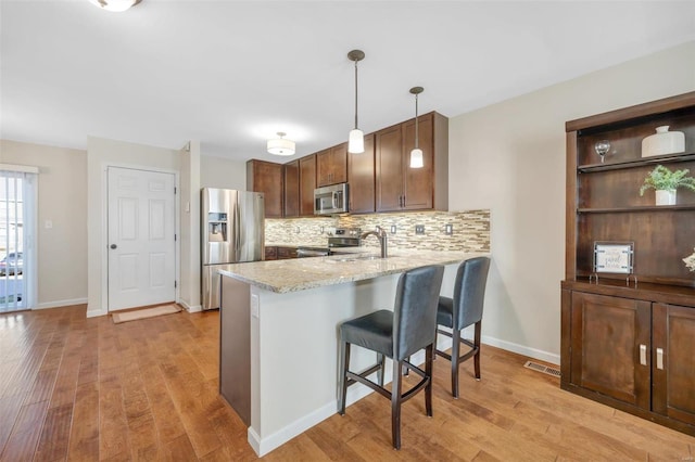 kitchen featuring light wood-type flooring, stainless steel appliances, tasteful backsplash, and a peninsula