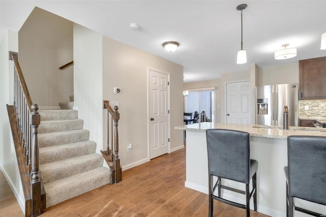 kitchen featuring a breakfast bar area, light wood finished floors, stainless steel fridge with ice dispenser, pendant lighting, and tasteful backsplash