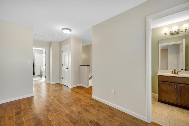 hallway with a sink, light wood-type flooring, an upstairs landing, and baseboards