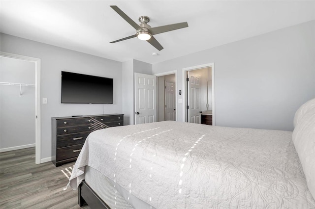 bedroom featuring wood finished floors, baseboards, ceiling fan, a closet, and a walk in closet