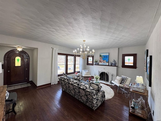 living room featuring a textured ceiling, a notable chandelier, dark wood-type flooring, baseboards, and a brick fireplace