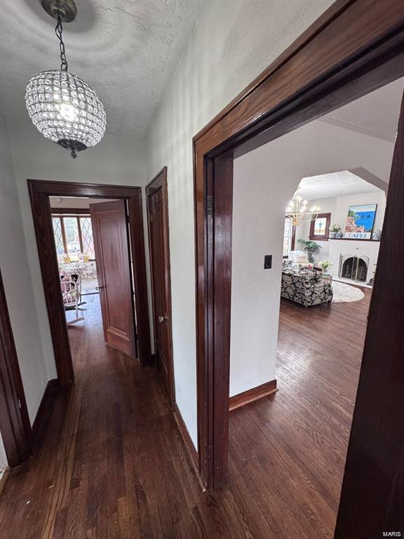 hall with a chandelier, dark wood-type flooring, vaulted ceiling, and a textured ceiling